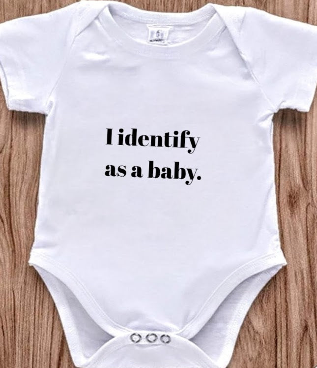 Funny baby onesie with the text 'I Identify as a baby' on a wooden background