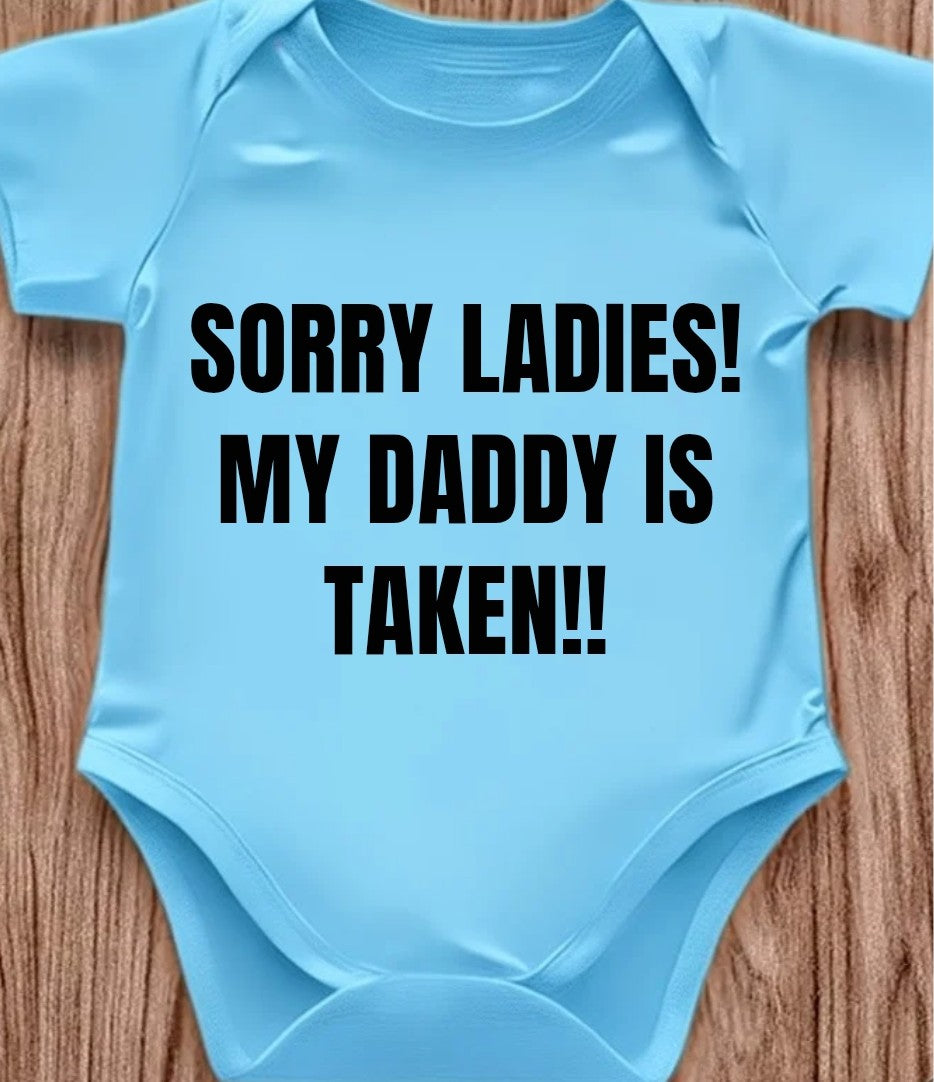 Funny baby onesie in blue with text saying 'SORRY LADIES! MY DADDY IS TAKEN!!' designed for laughs.
