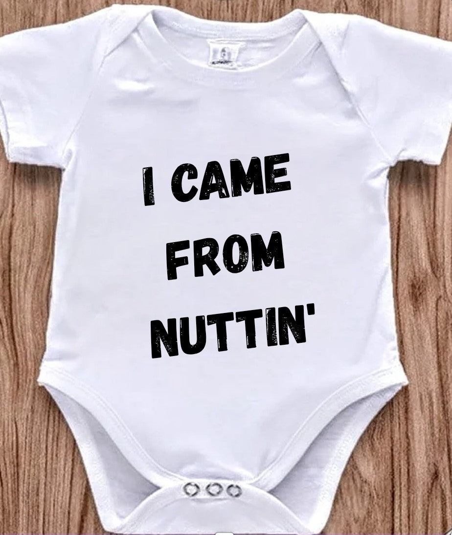 Funny baby onesie with the text 'I Came From Nuttin' on a wooden background