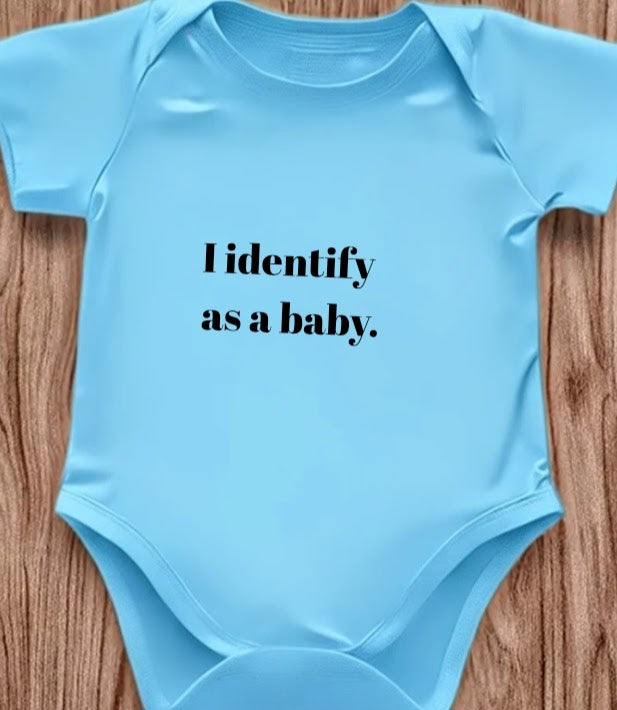 Funny baby onesie with the text 'I Identify as a baby' on a wooden background