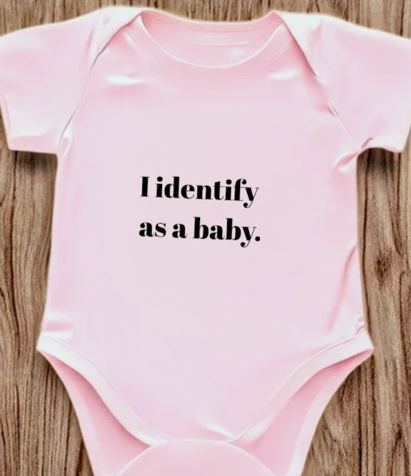 Funny baby onesie with the text 'I Identify as a baby' on a wooden background